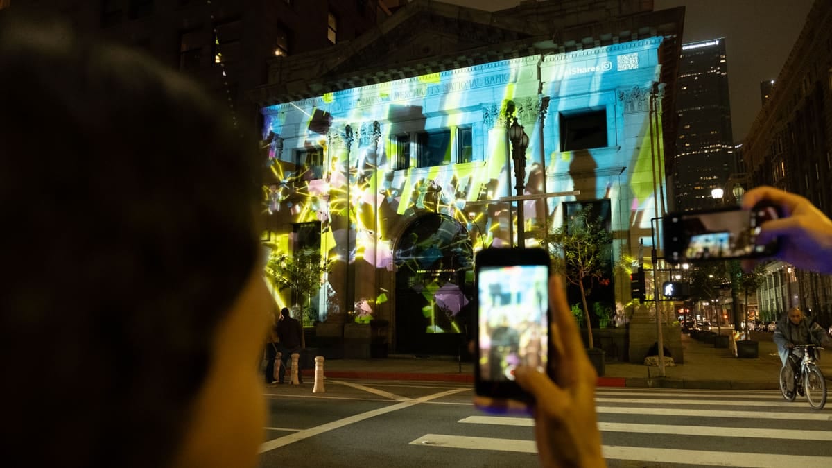 The iShares launch projection mapped onto a bank facade in Los Angeles at night, passersby filming on their phones.