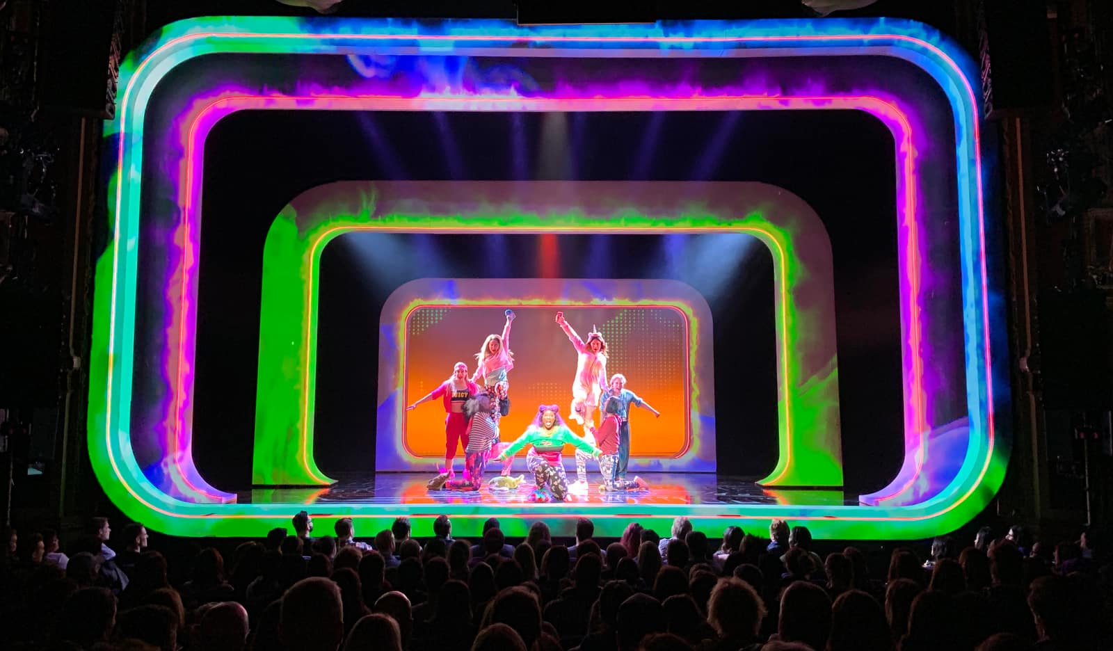 Be More Chill’s three portal frames outlined in concentric green, magenta and blue neon, the cast performing within on the Broadway stage.