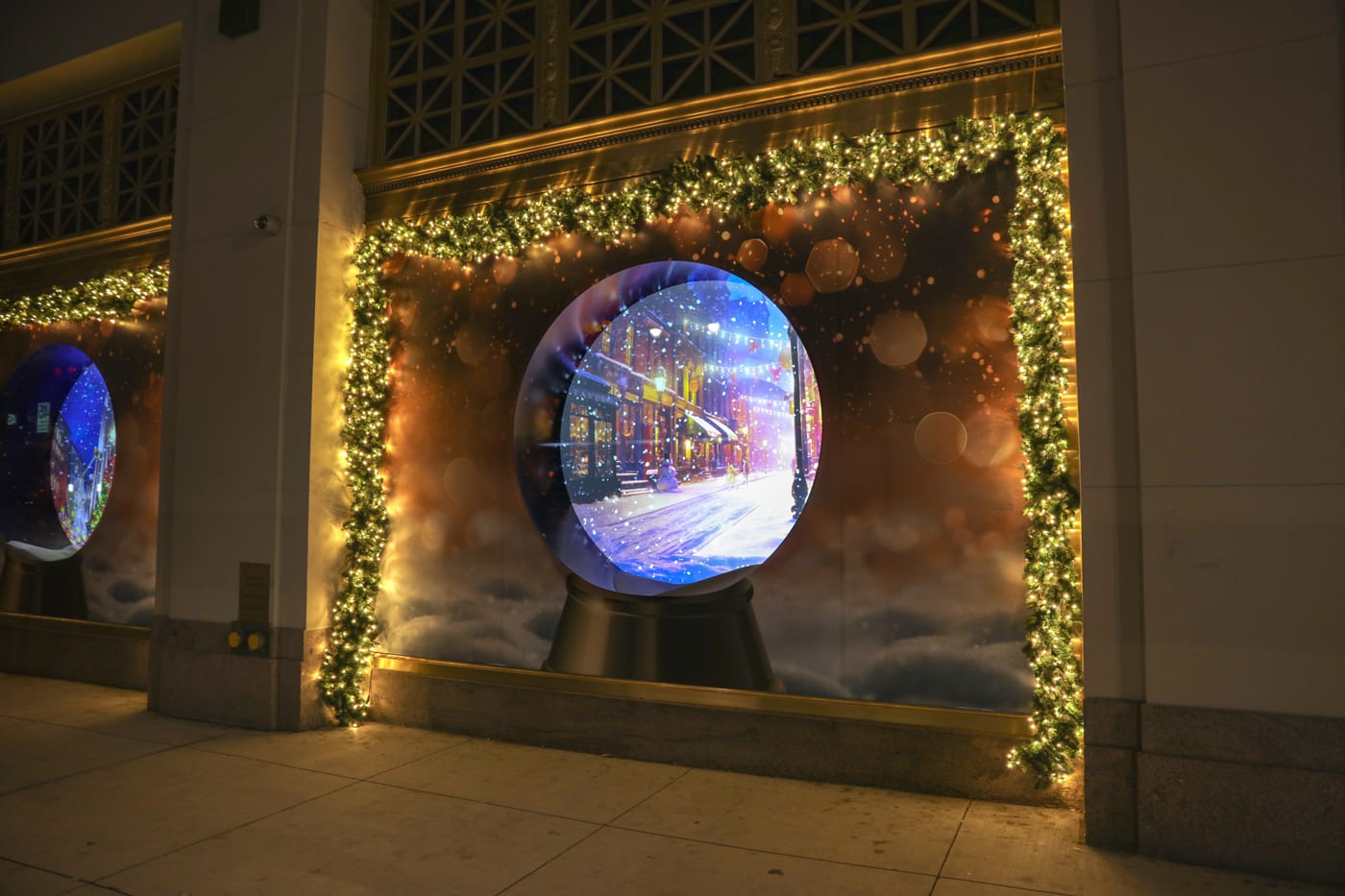 A glowing spherical display set into a garland-framed holiday window installation.