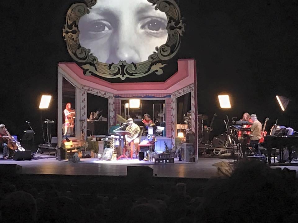 A face projected above an ornate proscenium set, the band performing below.