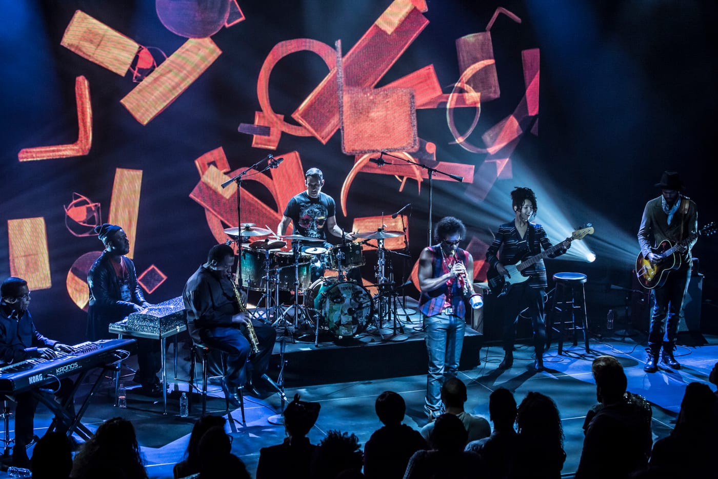 A concert stage under floating geometric set pieces, the band mid-performance.