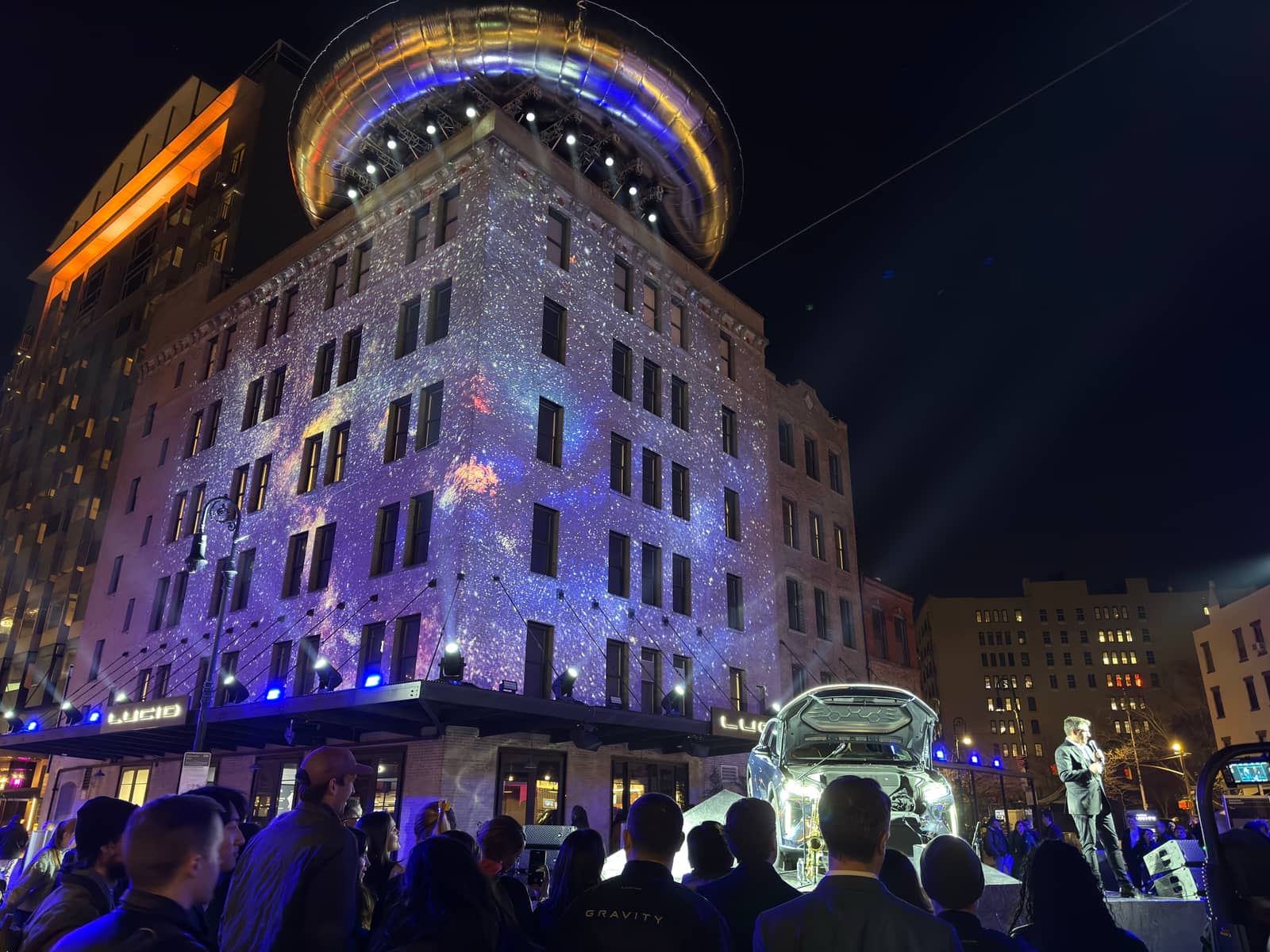 The cosmic projection over the facade during the reveal, a presenter and the Gravity SUV on the stage before the crowd.