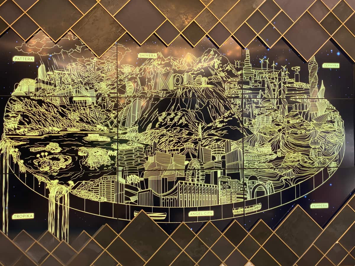 A gold line-art mural mapping the Modelland world across a wall — mountains, structures and pathways drawn in fine gold line.